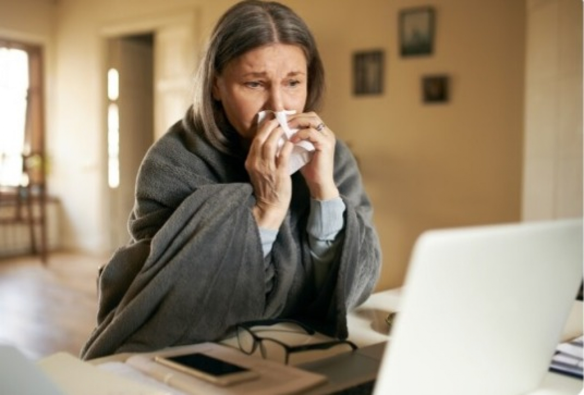 Mulher com sintomas de gripe em casa retrata os impactos das síndromes gripais no dia a dia.