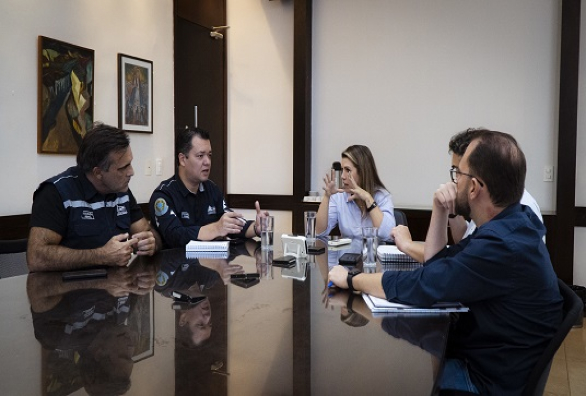 Grupo de pessoas participa de reunião em sala, discutindo e fazendo anotações.