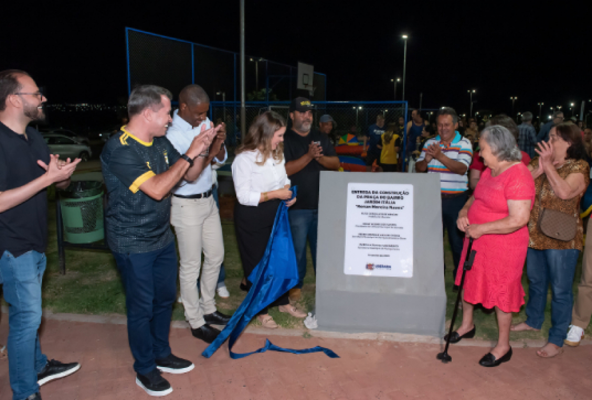 A imagem mostra um grupo de pessoas reunidas em um evento de inauguração, com uma placa sendo descerrada