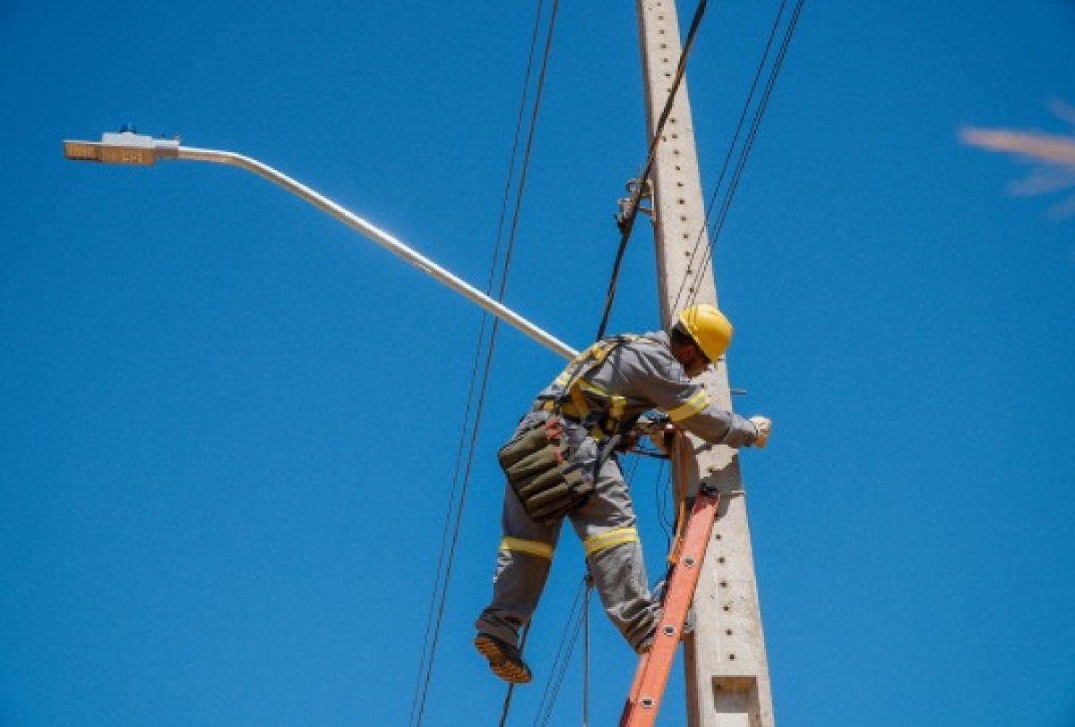 Um trabalhador em segurança realiza manutenção em sistemas elétricos em um poste de utilidade pública.