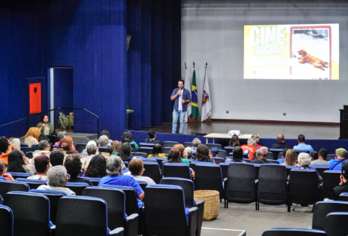 Público assiste a uma apresentação no auditório com projeção e palestra.