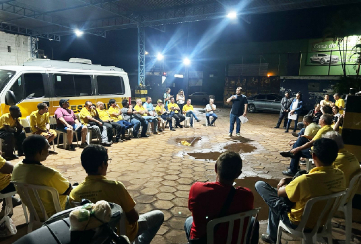 Roda de conversa noturna com participantes uniformizados, realizada em espaço aberto sob cobertura metálica.