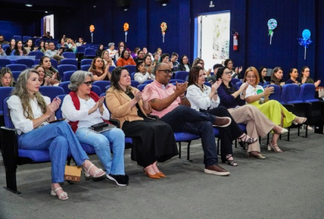 Público atento e engajado participa de evento em auditório, demonstrando apoio com aplausos.