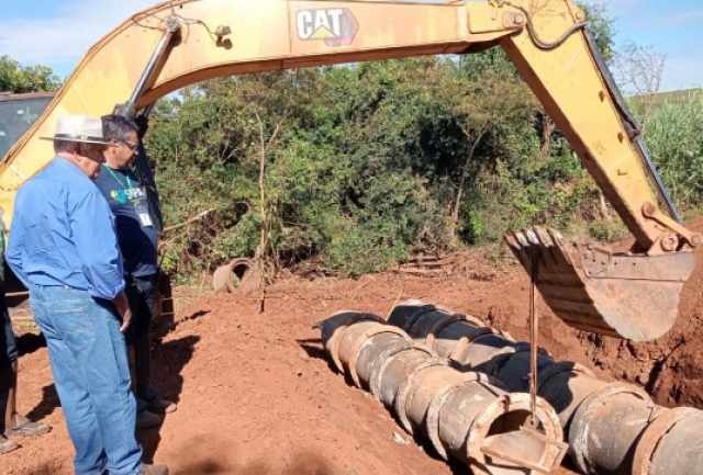 Supervisores acompanham a instalação de tubos de concreto com auxílio de uma escavadeira em obra de drenagem.