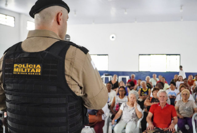 Policial militar de Minas Gerais realiza palestra para um público majoritariamente idoso em um ambiente comunitário.