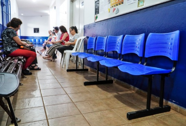 A imagem mostra uma sala de espera, várias pessoas estão sentadas. 