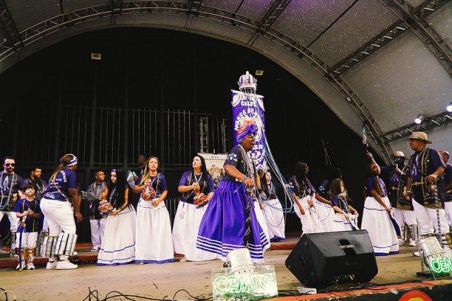 Grupo de pessoas apresenta uma manifestação cultural tradicional em um palco.